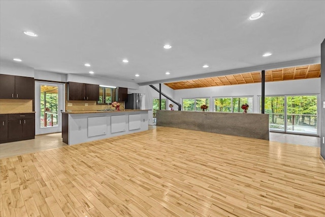 interior space with light wood-type flooring, dark brown cabinetry, a kitchen bar, and stainless steel fridge