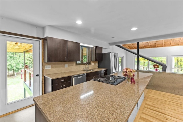 kitchen featuring appliances with stainless steel finishes, dark brown cabinetry, light stone counters, vaulted ceiling, and sink