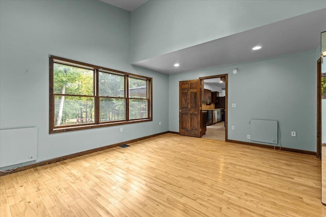 empty room with light wood-type flooring and a towering ceiling