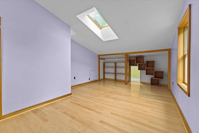 additional living space featuring vaulted ceiling with skylight and light hardwood / wood-style flooring