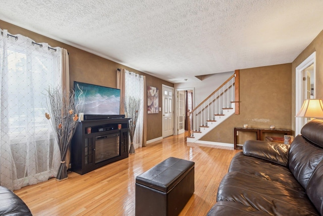 living area with stairs, a textured ceiling, wood finished floors, and baseboards