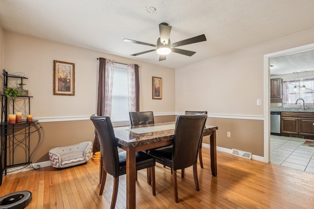 dining area featuring visible vents, baseboards, a ceiling fan, light wood-style flooring, and a textured ceiling