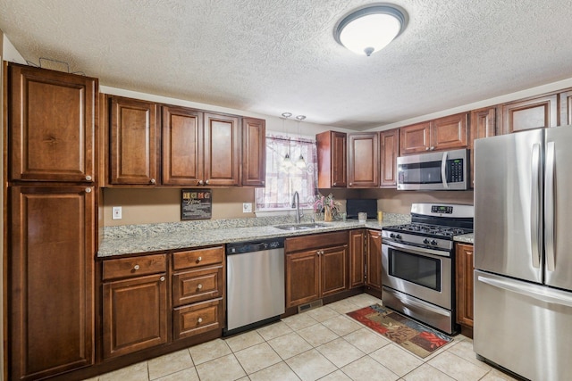 kitchen with light tile patterned floors, light stone counters, a sink, hanging light fixtures, and appliances with stainless steel finishes