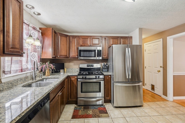 kitchen featuring light tile patterned floors, stainless steel appliances, a sink, light stone countertops, and pendant lighting