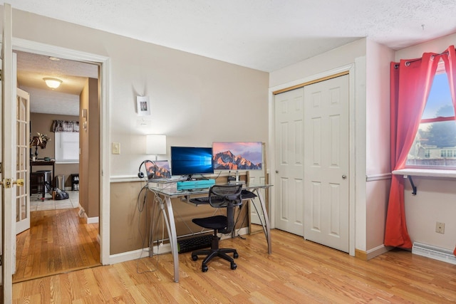 office featuring a textured ceiling, french doors, baseboards, and light wood-style floors