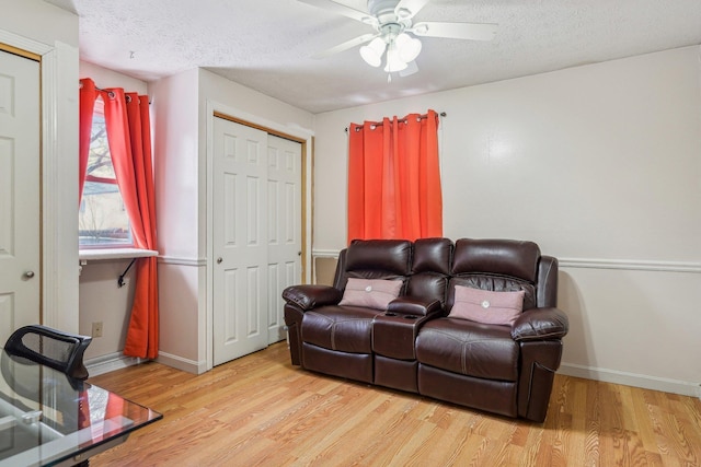 living area with baseboards, a textured ceiling, and light wood finished floors