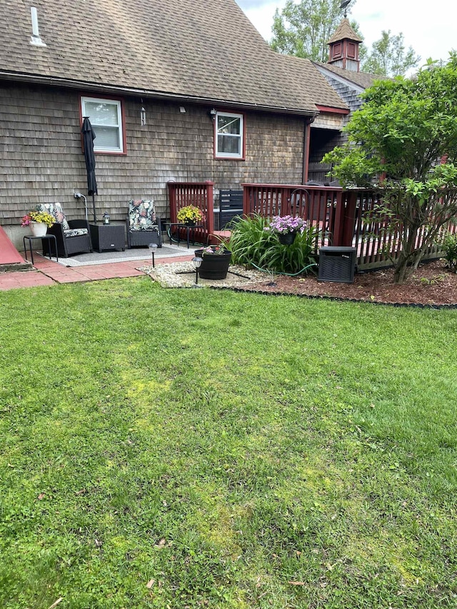 rear view of house featuring roof with shingles, a lawn, and a patio