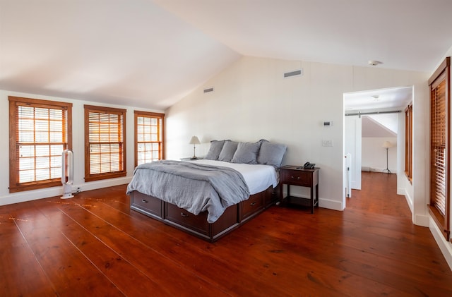 bedroom featuring a barn door, dark wood-type flooring, and vaulted ceiling