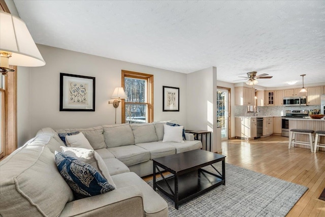 living room with ceiling fan, light hardwood / wood-style flooring, and a textured ceiling