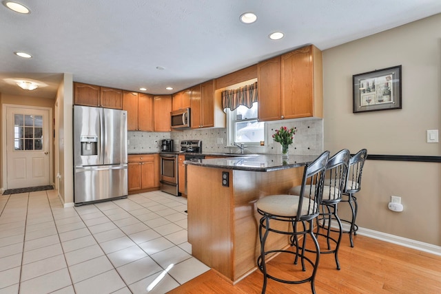 kitchen with a kitchen bar, appliances with stainless steel finishes, sink, backsplash, and kitchen peninsula