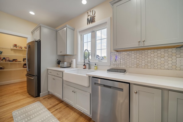 kitchen with stainless steel appliances, decorative backsplash, light hardwood / wood-style floors, gray cabinets, and sink