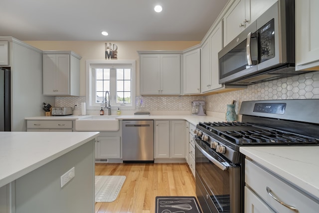 kitchen with stainless steel appliances, light stone countertops, light hardwood / wood-style floors, backsplash, and sink