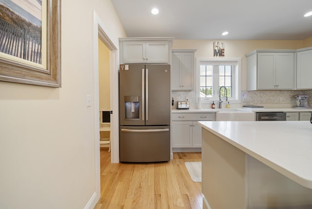 kitchen with stainless steel refrigerator with ice dispenser, light hardwood / wood-style floors, sink, white cabinets, and decorative backsplash