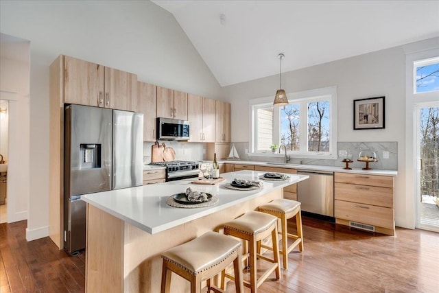 kitchen featuring appliances with stainless steel finishes, a breakfast bar area, decorative light fixtures, light brown cabinets, and a kitchen island