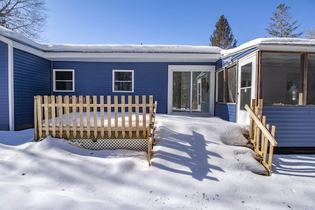 snow covered rear of property featuring a sunroom