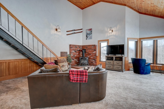 living area featuring a wood stove, light colored carpet, stairs, and wooden ceiling