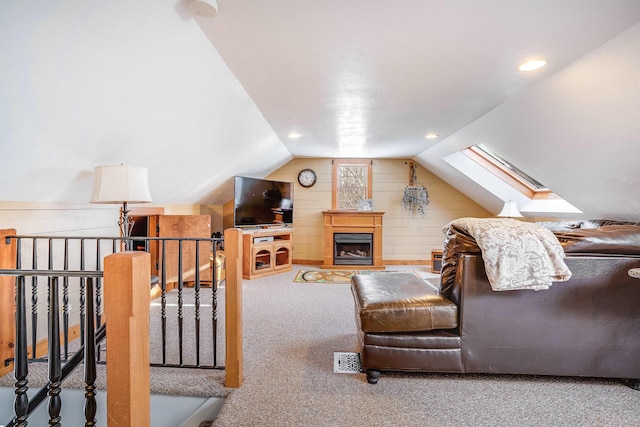 interior space with wooden walls, lofted ceiling with skylight, a fireplace, and carpet