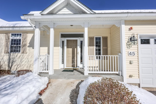 snow covered property entrance with a garage and covered porch