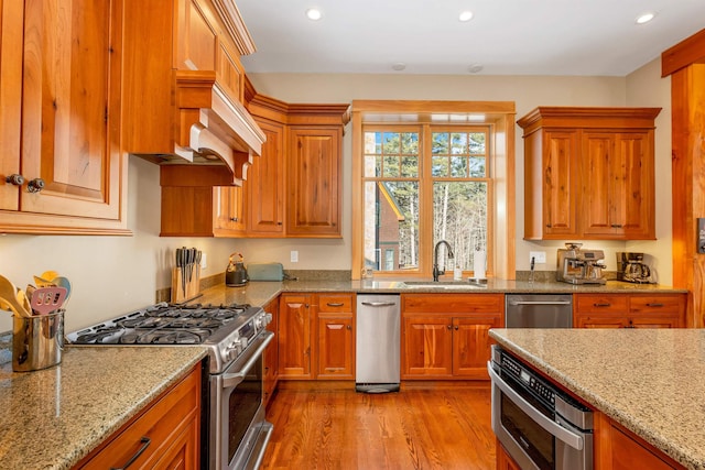 kitchen featuring stainless steel appliances, light wood-style floors, light stone countertops, and a sink