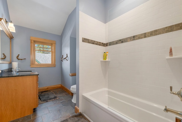 bathroom with vanity, baseboards, washtub / shower combination, stone tile flooring, and toilet