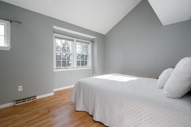 bedroom with baseboards, light wood finished floors, visible vents, and vaulted ceiling