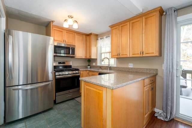 kitchen with appliances with stainless steel finishes, dark tile patterned flooring, light brown cabinetry, a sink, and light stone counters