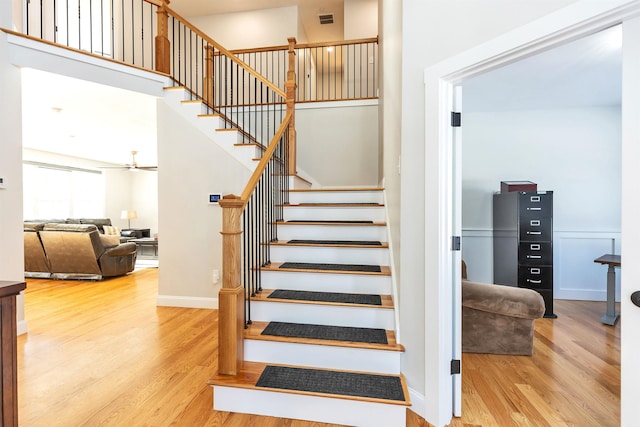 staircase featuring a towering ceiling, visible vents, and wood finished floors