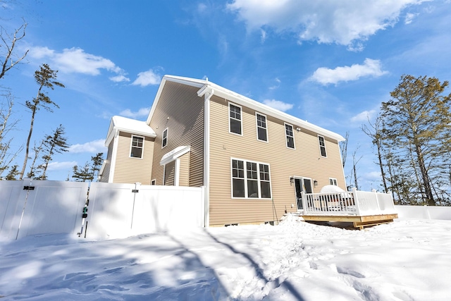 snow covered back of property with a gate, a wooden deck, and fence