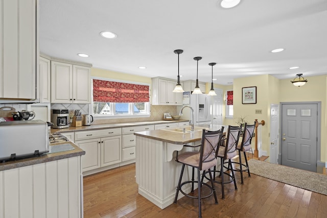 kitchen with a kitchen breakfast bar, decorative light fixtures, a kitchen island with sink, white fridge with ice dispenser, and a sink