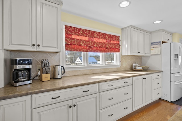 kitchen featuring tasteful backsplash, light wood-type flooring, white refrigerator with ice dispenser, and white cabinets