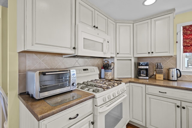 kitchen featuring dark countertops, white appliances, and white cabinetry