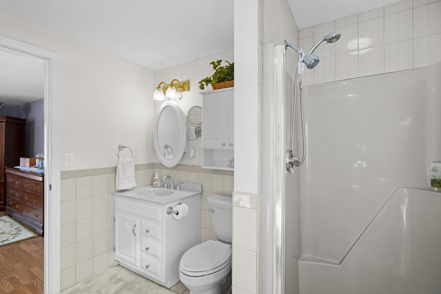 bathroom with toilet, a shower, vanity, and tile walls