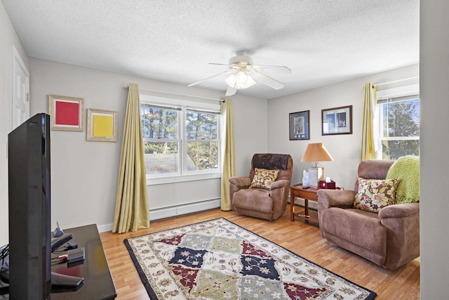 sitting room featuring a baseboard heating unit, ceiling fan, light wood-type flooring, and plenty of natural light