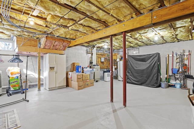 basement featuring white refrigerator with ice dispenser, water heater, and visible vents