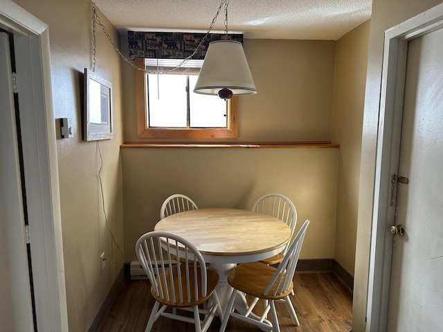 dining space with a textured ceiling, baseboards, and wood finished floors