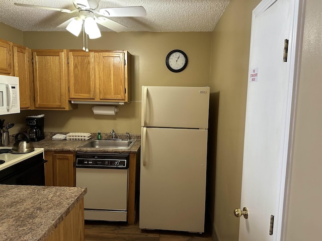 kitchen featuring white appliances, dark countertops, a sink, and brown cabinets