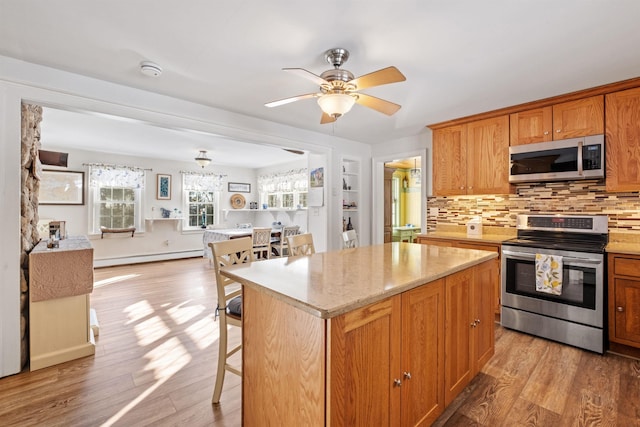 kitchen featuring a center island, stainless steel appliances, brown cabinetry, open floor plan, and a kitchen bar