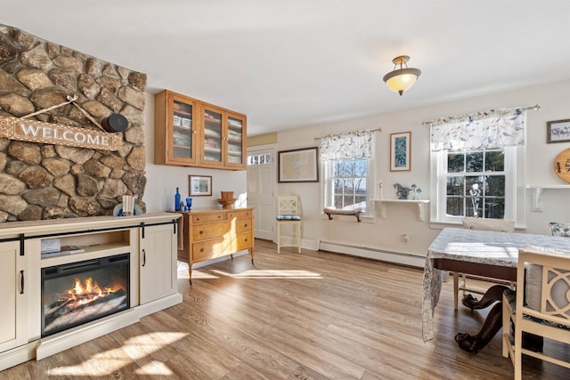 interior space featuring a baseboard heating unit, light wood finished floors, and a glass covered fireplace