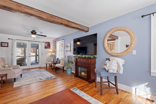 living area with ceiling fan, beamed ceiling, wood finished floors, and a glass covered fireplace