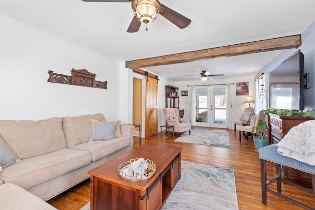 living area featuring ceiling fan, a barn door, french doors, light wood-type flooring, and beamed ceiling