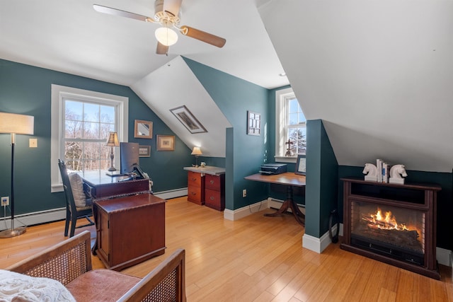 office space with lofted ceiling, baseboard heating, light wood-style floors, a glass covered fireplace, and baseboards