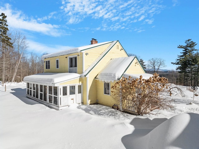 snow covered rear of property with a chimney and a sunroom