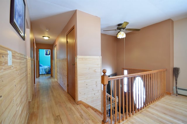 corridor featuring light wood-style flooring, a baseboard heating unit, and an upstairs landing