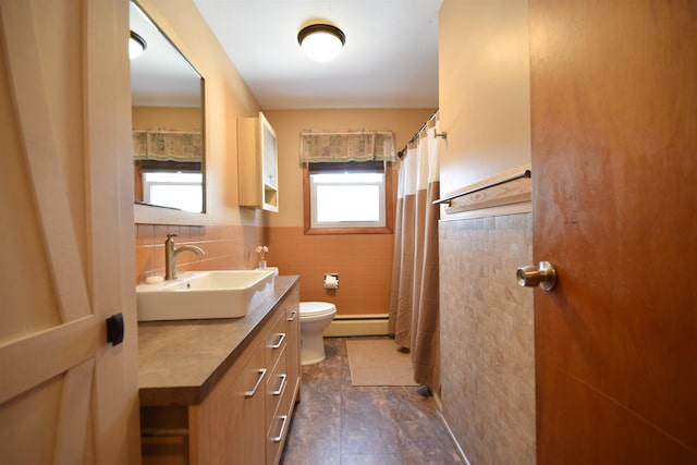 full bathroom featuring tile walls, toilet, baseboard heating, wainscoting, and vanity