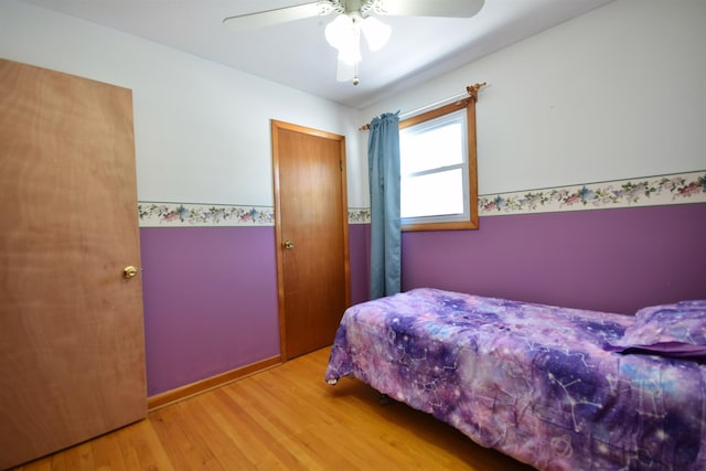 bedroom featuring a wainscoted wall, light wood-style flooring, and a ceiling fan