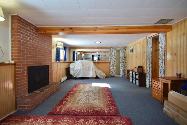 living room featuring dark colored carpet, visible vents, baseboard heating, a brick fireplace, and wooden walls