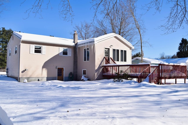 snow covered back of property with a chimney and a wooden deck