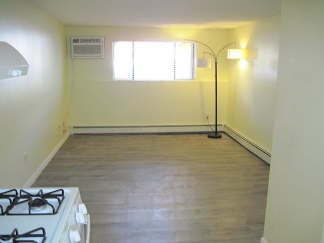 unfurnished room with baseboard heating, a wall mounted air conditioner, wood finished floors, and baseboards