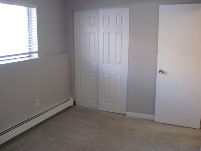 unfurnished bedroom featuring baseboard heating, carpet, and a closet