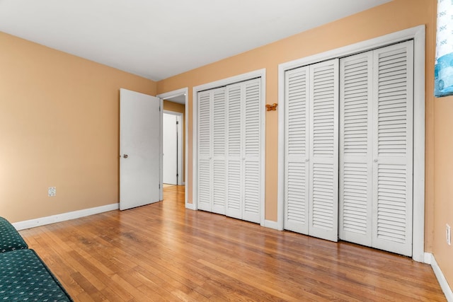 unfurnished bedroom with light wood finished floors, baseboards, and two closets